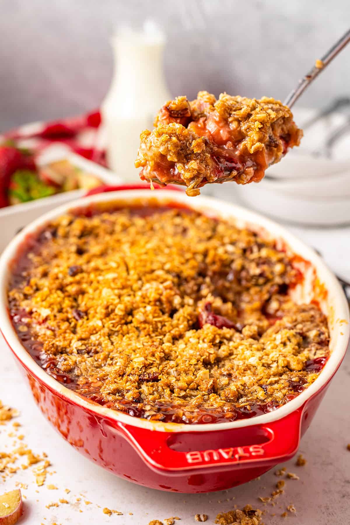 A bowl of strawberry rhubarb crisp with a spoon lifting some up, showing the jammy insides. 