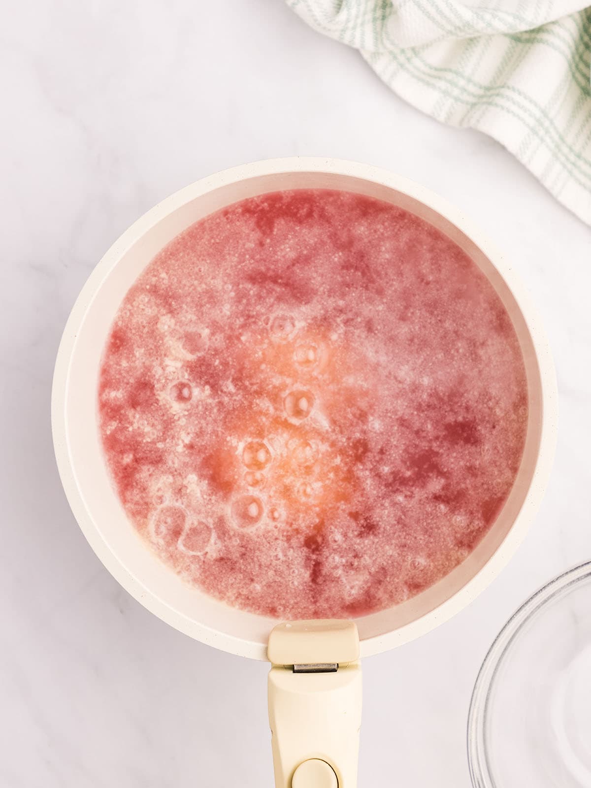 Wild violet jelly boiling in a white pot, top view. 