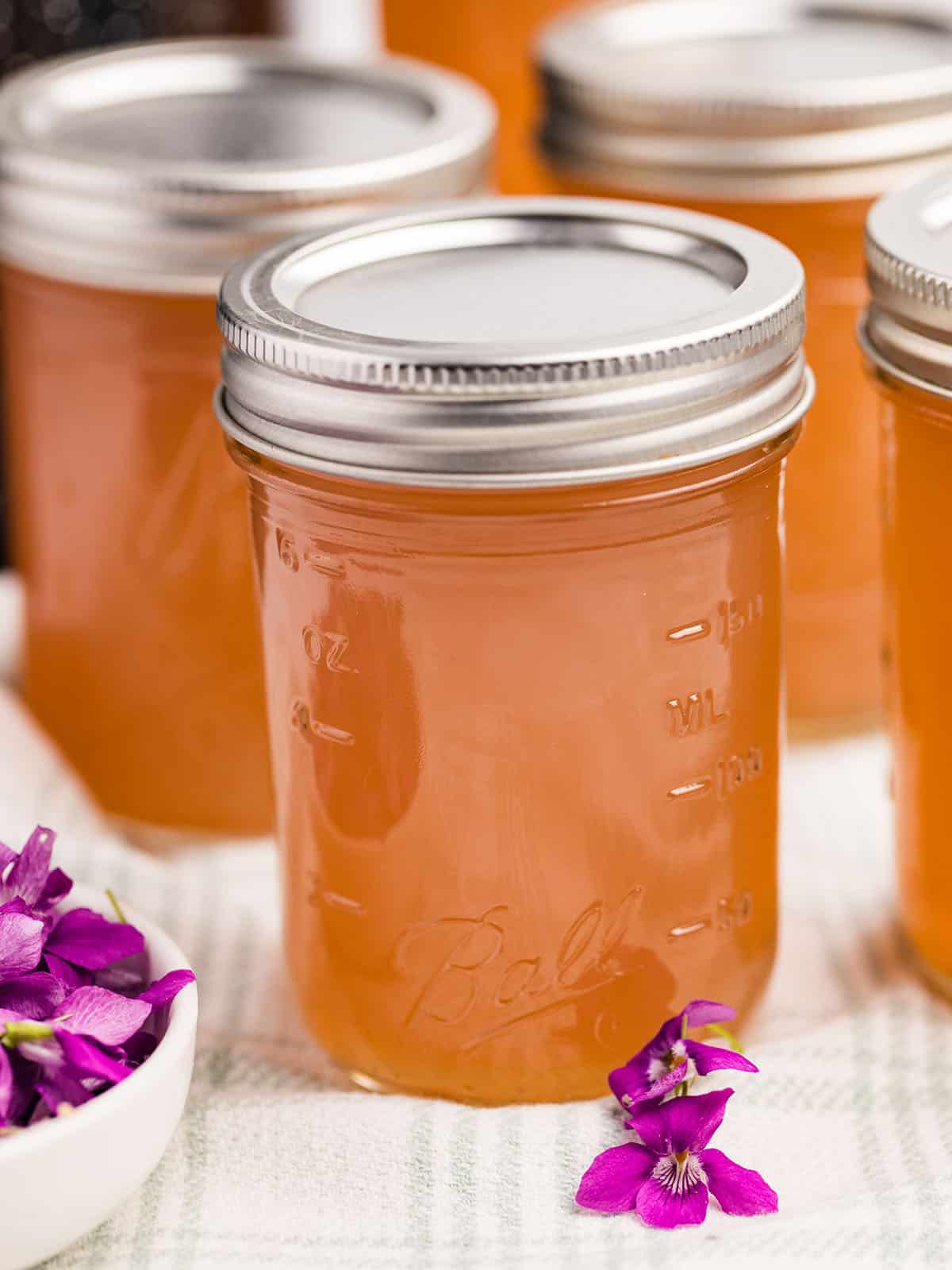 Jars of low sugar wild violet jelly, with fresh violet flowers surrounding. 