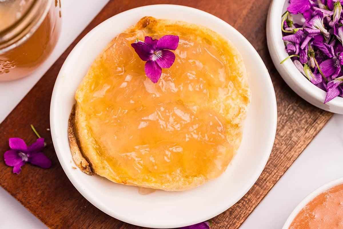Wild violet jelly spread on a pancake with a fresh violet flower on it as well as in a bowl to the side. 