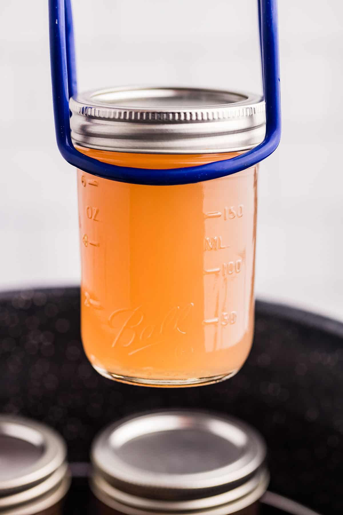 A jar lifter holding a jar of violet jelly above the canning pot. 