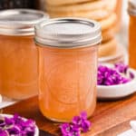 Wild violet jelly that is pink, on a wood surface surrounded by fresh violet flowers.