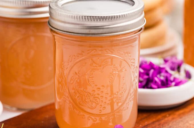 Wild violet jelly that is pink, on a wood surface surrounded by fresh violet flowers.