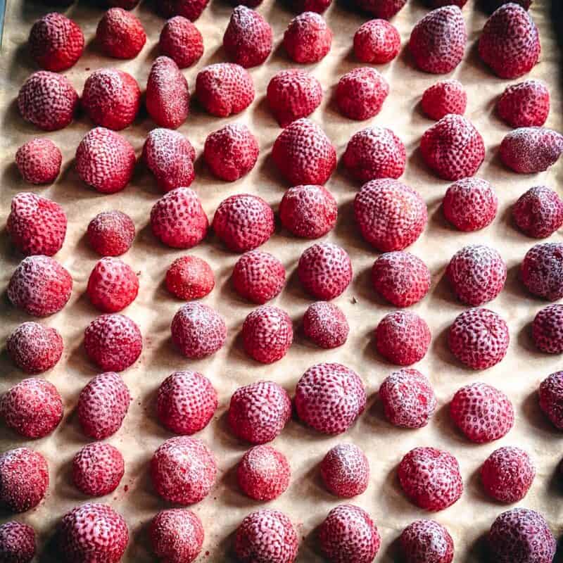 A baking sheet of frozen strawberries on parchment paper.