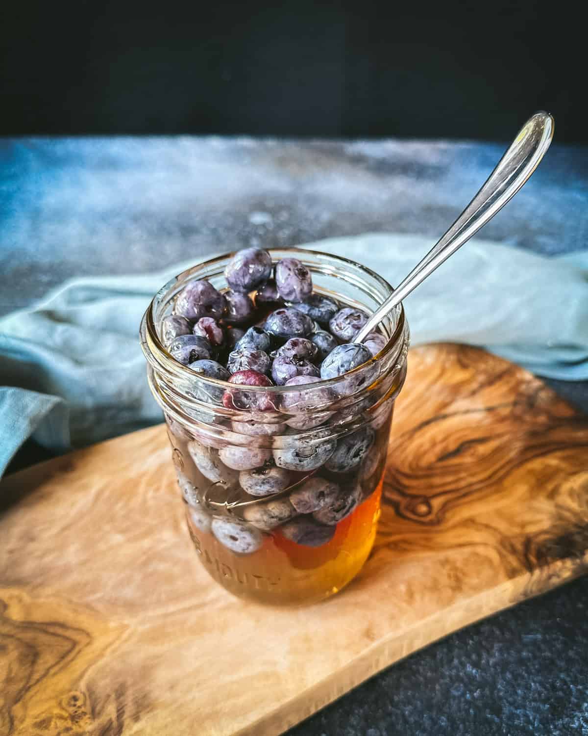 A jar of fermented honey blueberries on a wood surface. 